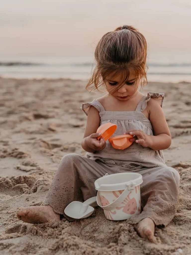 Klein meisje speelt met strandvormpjes in het zand bij zonsondergang tijdens een familieshoot op het strand van Den Haag