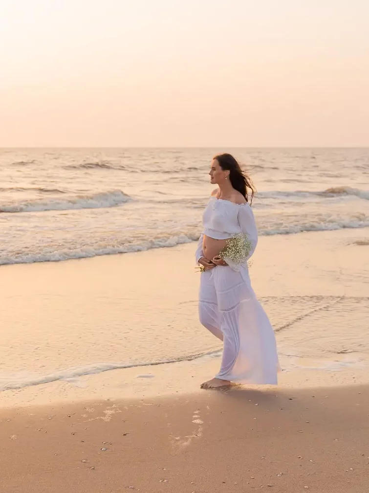 Zwangere vrouw wandelt dromerig bij zonsondergang over het strand met de zee op de achtergrond