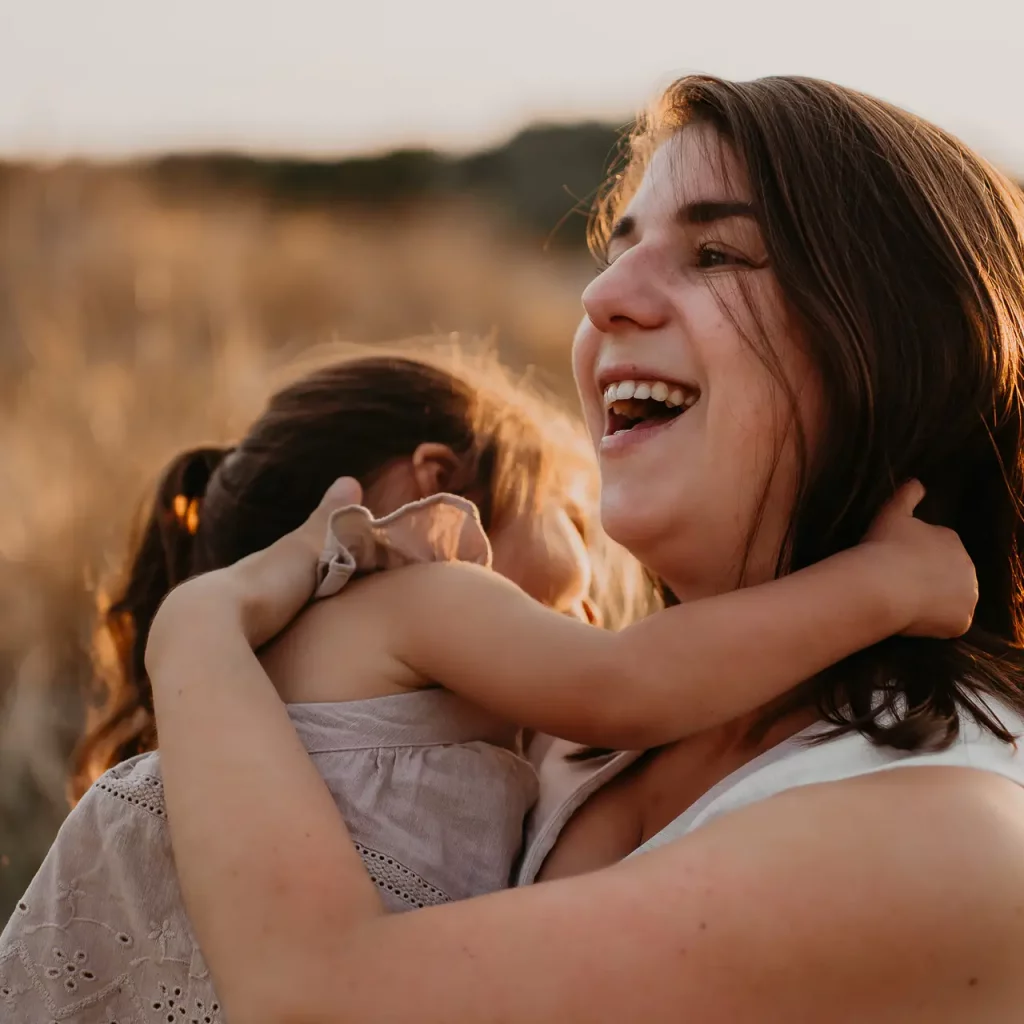 Moeder lachend met haar dochter op arm in de duinen tijdens een gezinsfotoshoot in Den Haag