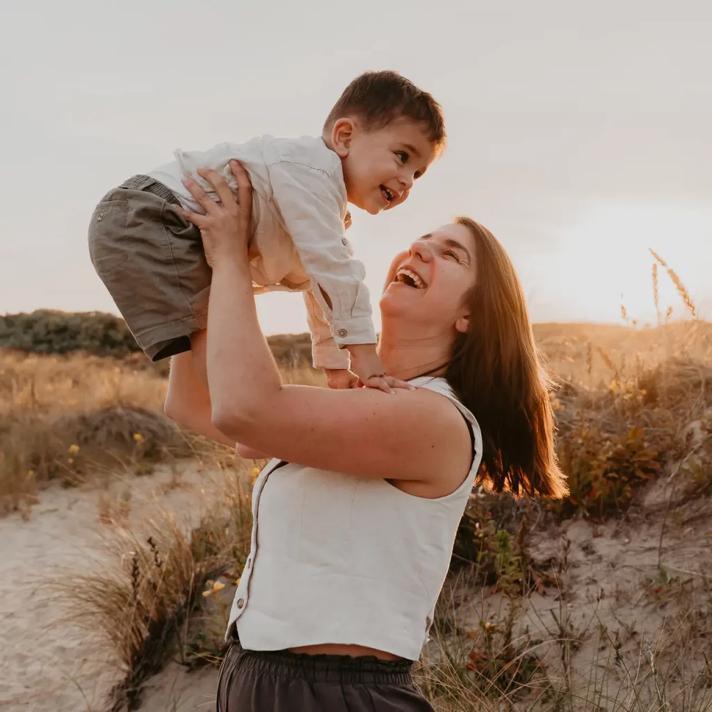 Moeder gooit haar zoon lachend in de lucht in de duinen tijdens een gezinsfotoshoot in Den Haag